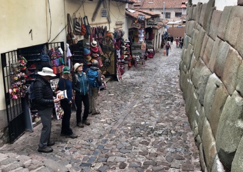 Turistas viendo muro de piedra Inca y tiendas vendiendo tesoros turísticos Cuzco, 2017.