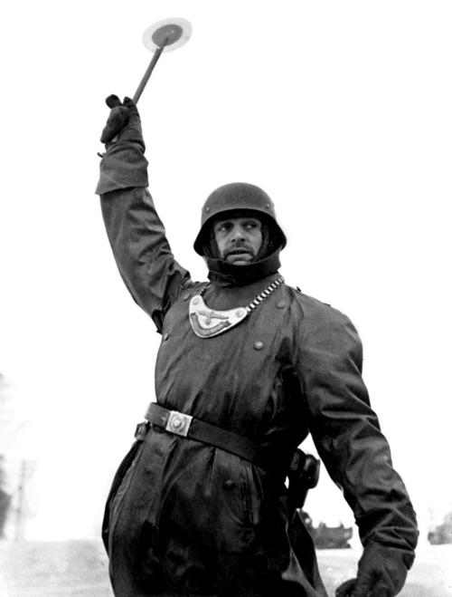 A German Wehrmacht soldier of the Feldgendarmerie (military police) directs military transport durin