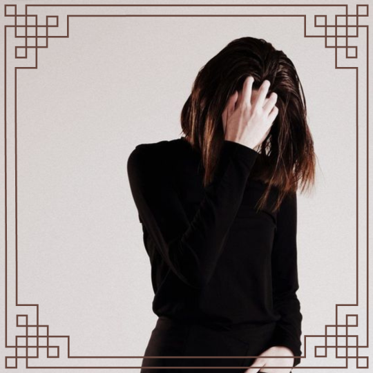 An image of a woman with short dark hair covering her face by holding her head and looking down with dark reddish brown lines interlocking around the border