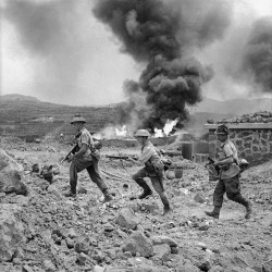 warpicshistory:Pantelleria and Lampedusa May - June 1943: Men of 1st Battalion, The Duke of Wellington’s Regiment, advance past a burning fuel store on Pantelleria. Left to right: Lance Sergeant A Haywood, Private C Norman and Private H Maw. #war #history