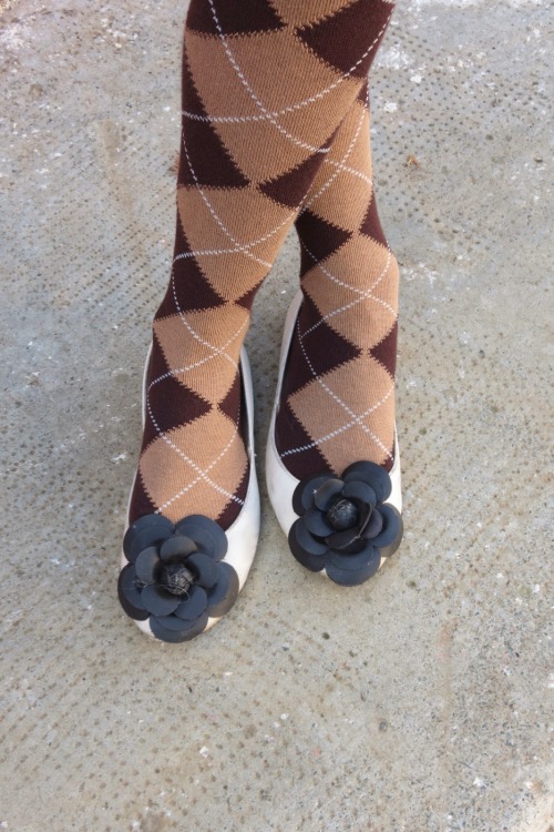Detail of brown diamond patterned wool tights and flat white shoes with black flower detail