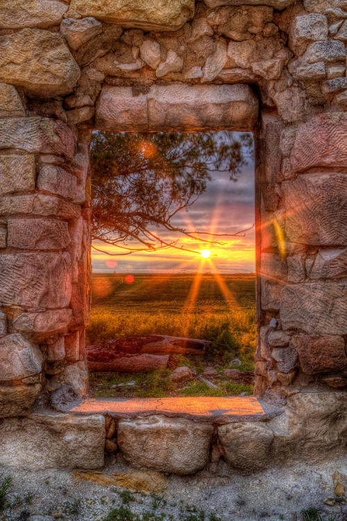 “A Kansas sunset throuh the window of an abandoned and forgotten limestone house in Ellis Coun