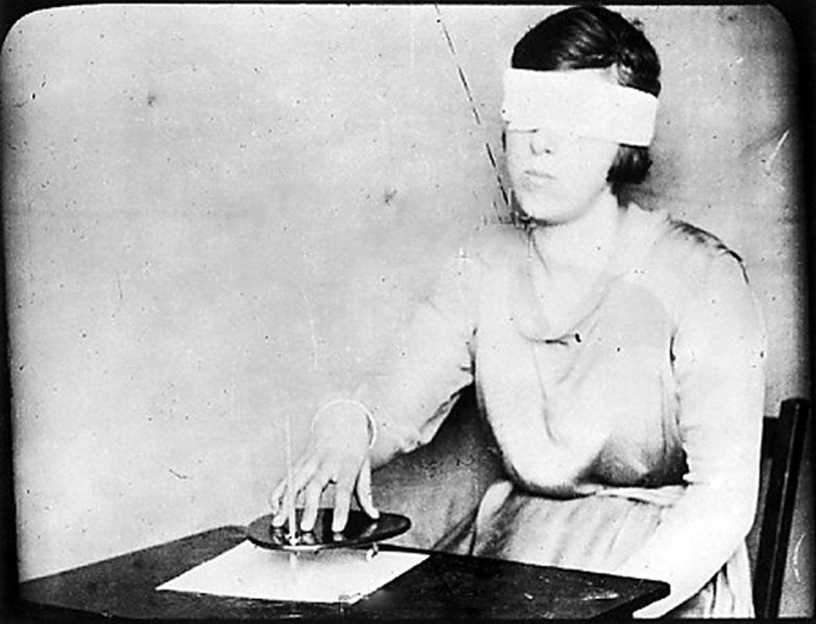 Mary Evans - A girl, blindfolded, uses the planchette with a pencil fixed in it,