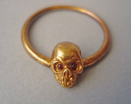 A 19th century gold mourning ring. The bezel is shaped like a skull with red enamel eyes, and has th