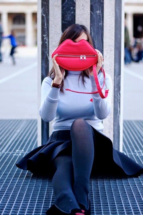 Black tights, pleated skirt and light grey top with red lip shaped purse