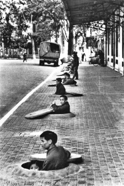 severinar:  During an air raid alert, residents of Hanoi wait in chest-deep sidewalk shelters for the all-clear signal. This photo was taken by the first American photographer since 1954 permitted to report on daily life in the capital of North Vietnam,