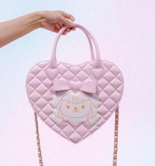 A pink heart shaped purse with
a white and gold design of a
stylized lop-bunny printed on the
front. There is a bow with a heart
above the decal. The purse has a
diamond grid pattern embroidered
on it with a gold chain strap for the
shoulder.