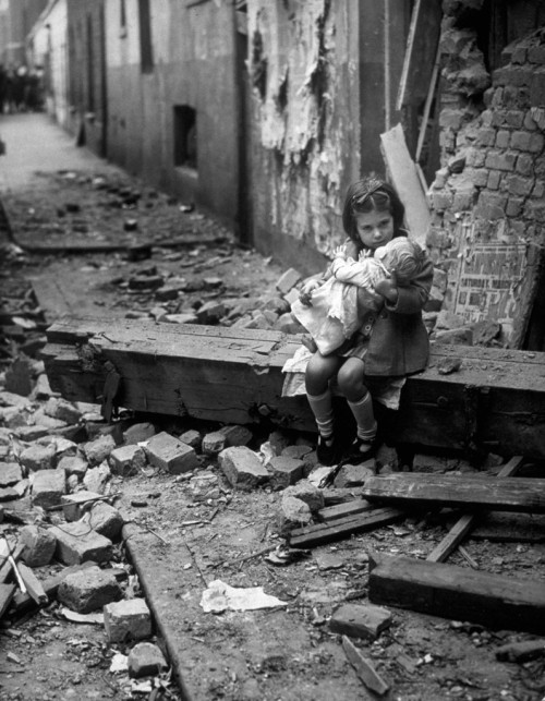 vintageeveryday:A little English girl comforts her doll in the rubble of her bomb damaged home in 19