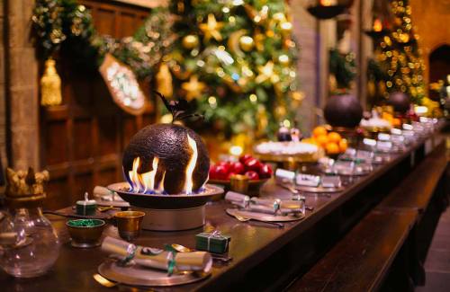 Gifts and crackers decorated for Slytherin House lined up along flaming Christmas puddings in readin