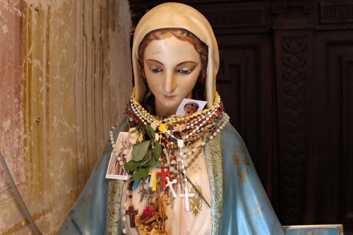 Devotional statue of the Blessed Virgin, festooned with Rosaries, santini, and ex votos. Norcia, Umb