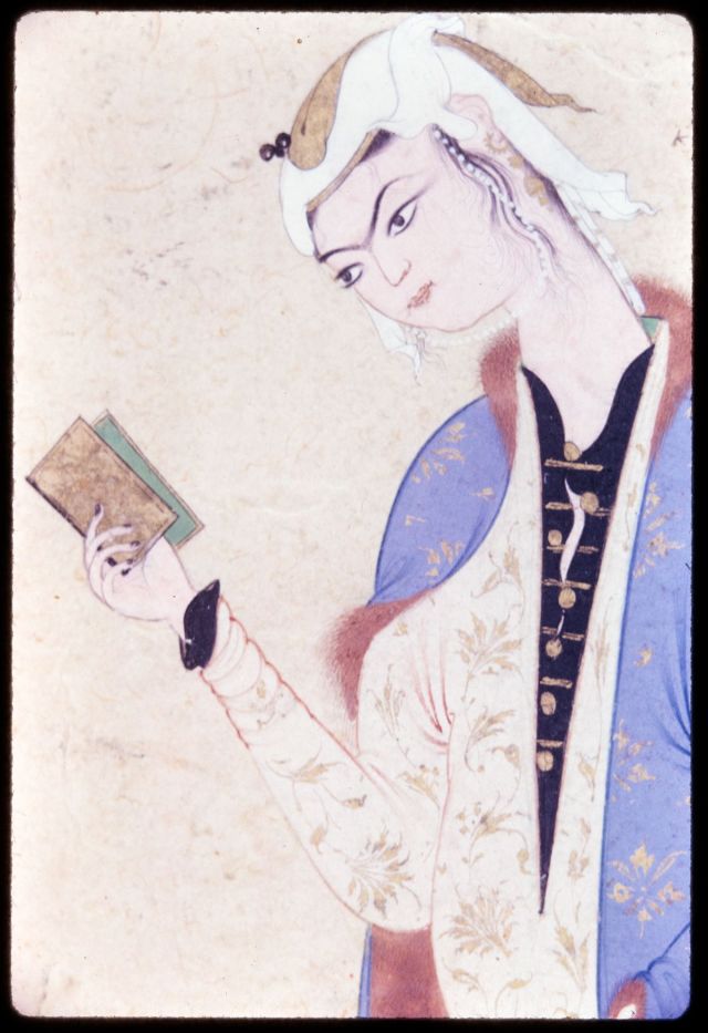 A girl with a white head scarf and a purple robe is holding a small book in her right hand and reading.