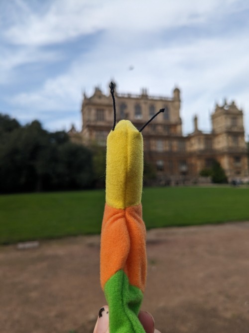 An inch worm beanie baby facing an old mansion, the sky is blue but scattered with white clouds
