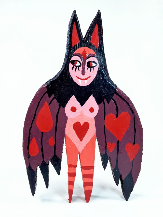 a flat wooden cut-out sculpture of a vampire that looks like a half-bat half-woman, in shades of black, dark purple, and red. her hair is long and dark, and her wings are painted with red hearts and red blood drops. 