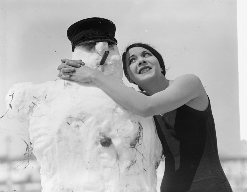 vintageeveryday:  Miss Fritzi Ridgeway does her best to try and melt this happy looking snowman, April 2, 1924.