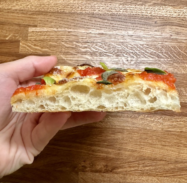 Sideways view of a fluffy, thin pizza slice.