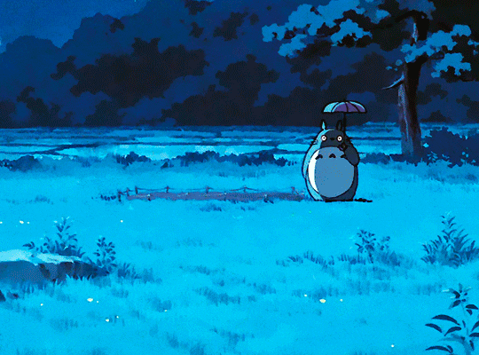 gifset of a scene from My Neighbor Totoro (1988). Totoro and his small Totoro friends walk on a field. Totoro is holding an umbrella. they eventually jump above a small crop, then turn around it to jump over it again. end ID.