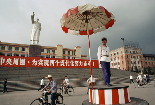 Chinese cyclists ride their bicycles through a square in Chengdu, July 1981.Photograph by Jodi Cobb,