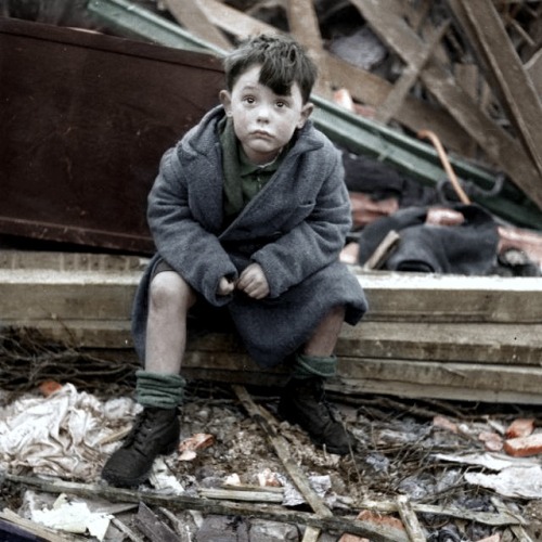 An orphaned boy sits amongst the debris of his home after his parents are killed in a V-2 rocket att