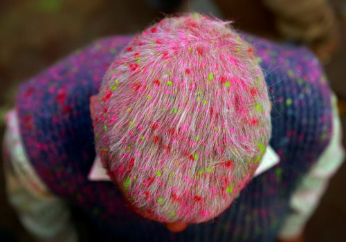 A Hindu devotee is covered in colored powder as he stands outside a temple during the religious fest