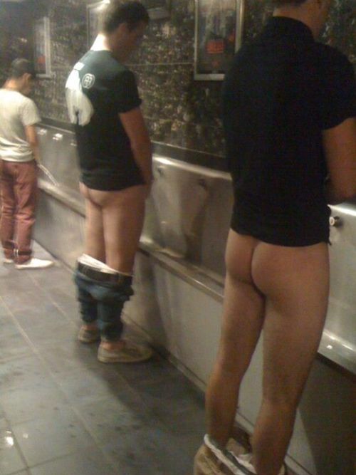 A couple of lads pissing in a trough urinal, with their pants down