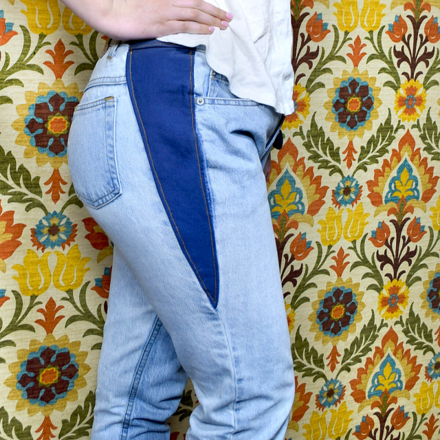 A close-up of a pair of light blue jeans with a dark blue denim insert at the waist.