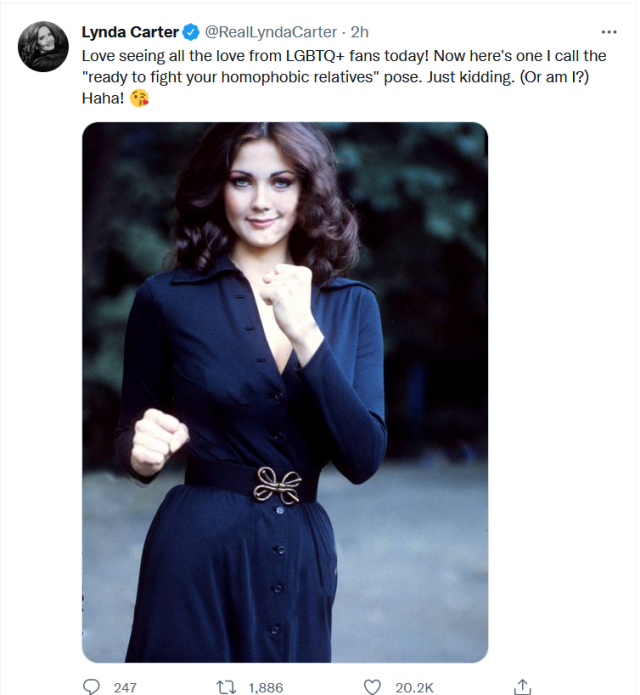 Tweet from @RealLyndaCarter dated June 1, 2022. Includes a vintage photo of Carter wearing a dark blue dress and striking the classic Wonder Woman pose with fists raised. Text reads: "Love seeing all the love from LGBTQ+ fans today! Now here's one I call the "ready to fight your homophobic relatives" pose. Just kidding. (Or am I?) Haha! "