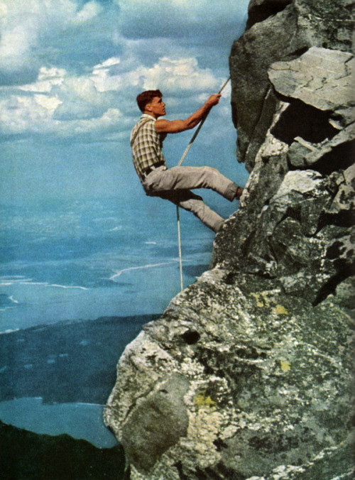 Life hanging by a slender rope, Frank Craighead rappels down the rock face of Mount St. John. Below 