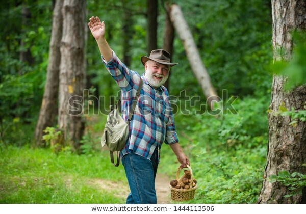 Old bearded man waving at the camera and holding a basket of mushrooms. 