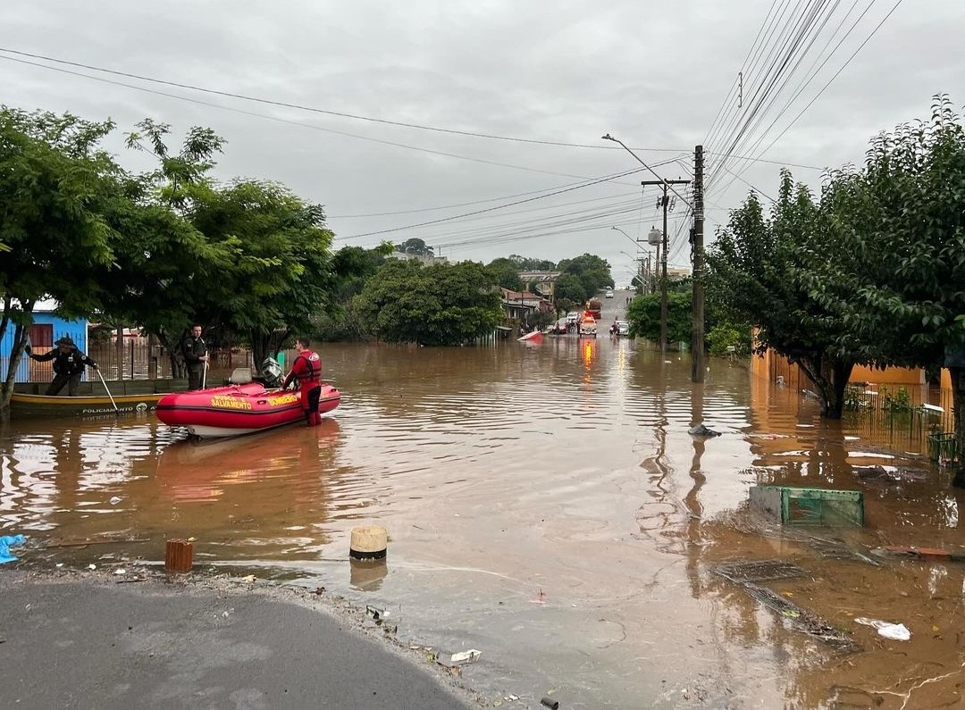 Picture taken in the city of Rio Pardo. A street is flooded and a fireman and a policeman are preparing a boat for rescue. Another policeman is maneuvering another boat in the background.