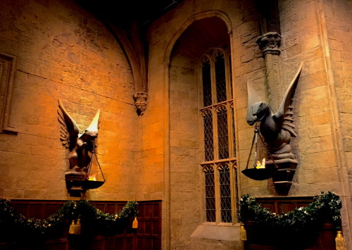 Christmas garlands decorate the Hogwarts Great Hall at Christmastime, hung below flambeau depicting 