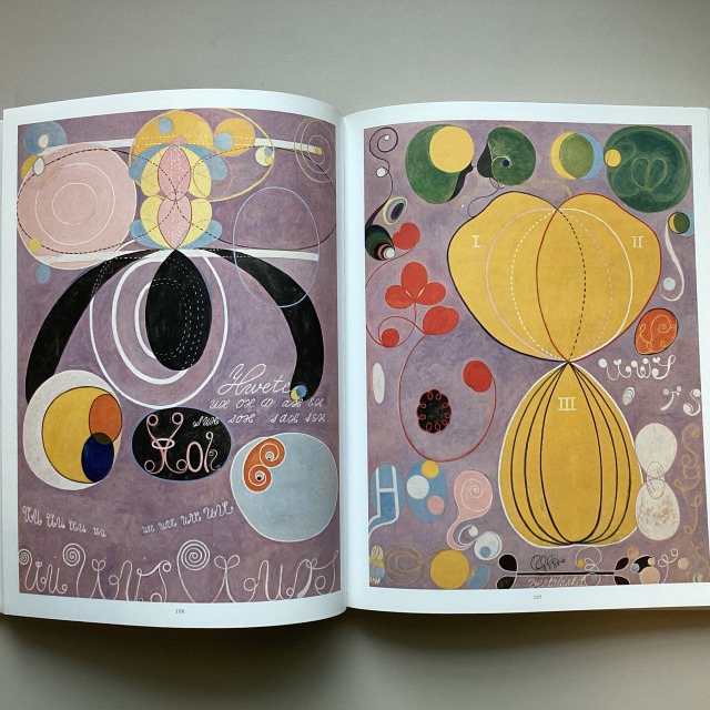 Left page shows many circular shapes and some oval or teardrop shapes painted in pale pink, yellow, pale blue, black, and orange along with some writings against a pink background. Right page shows organic shapes in yellow occupies more than half of the canvas. Many smaller circular and oval shapes in green, pink, blue, and white surround them. Many curves lines and some writings against a pink background. 