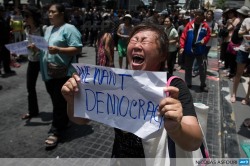afp-photo:  THAILAND, Bangkok : An anti coup protester screams at soldiers (not seen) as she holds a piece of paper that reads “we want democracy” during a planned gathering in Bangkok on May 25, 2014. Thailand’s military junta said it had disbanded