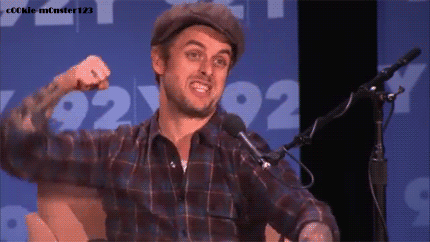 Gif of Billie Joe Armstrong, a white man in a plaid shirt, raises a fist in celebration, but he stops just before the fist pump to tilt his head in apparent confusion.