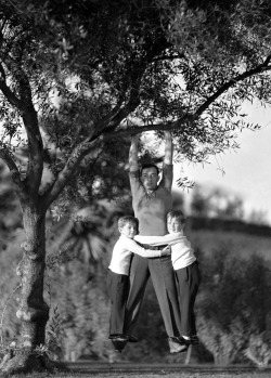 back-then:  Buster Keaton hanging from the branch of a tree with his two sons clinging onto his legs  October 1928 