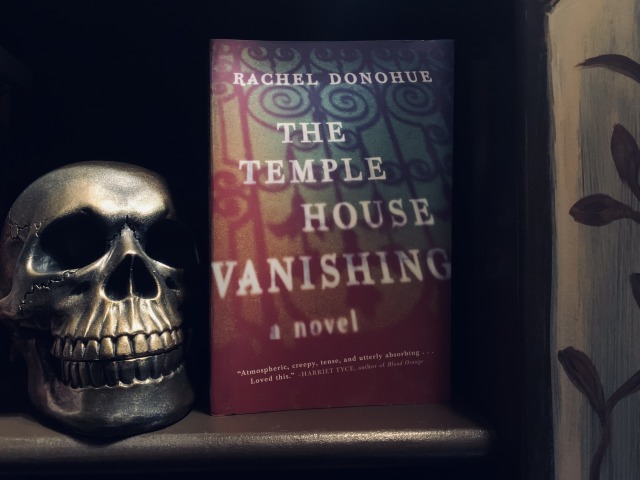 Shown is a skull in a bookcase with a copy of THE TEMPLE HOUSE VANISHING, with cover art depicting wrought-iron gates. Photo by AHS.