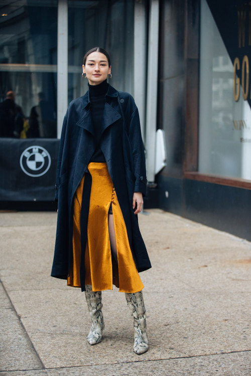 streetofstyle:Bruna Tenorio Bruna Tenorio wears a black trench coat, orange pleated skirt, and white