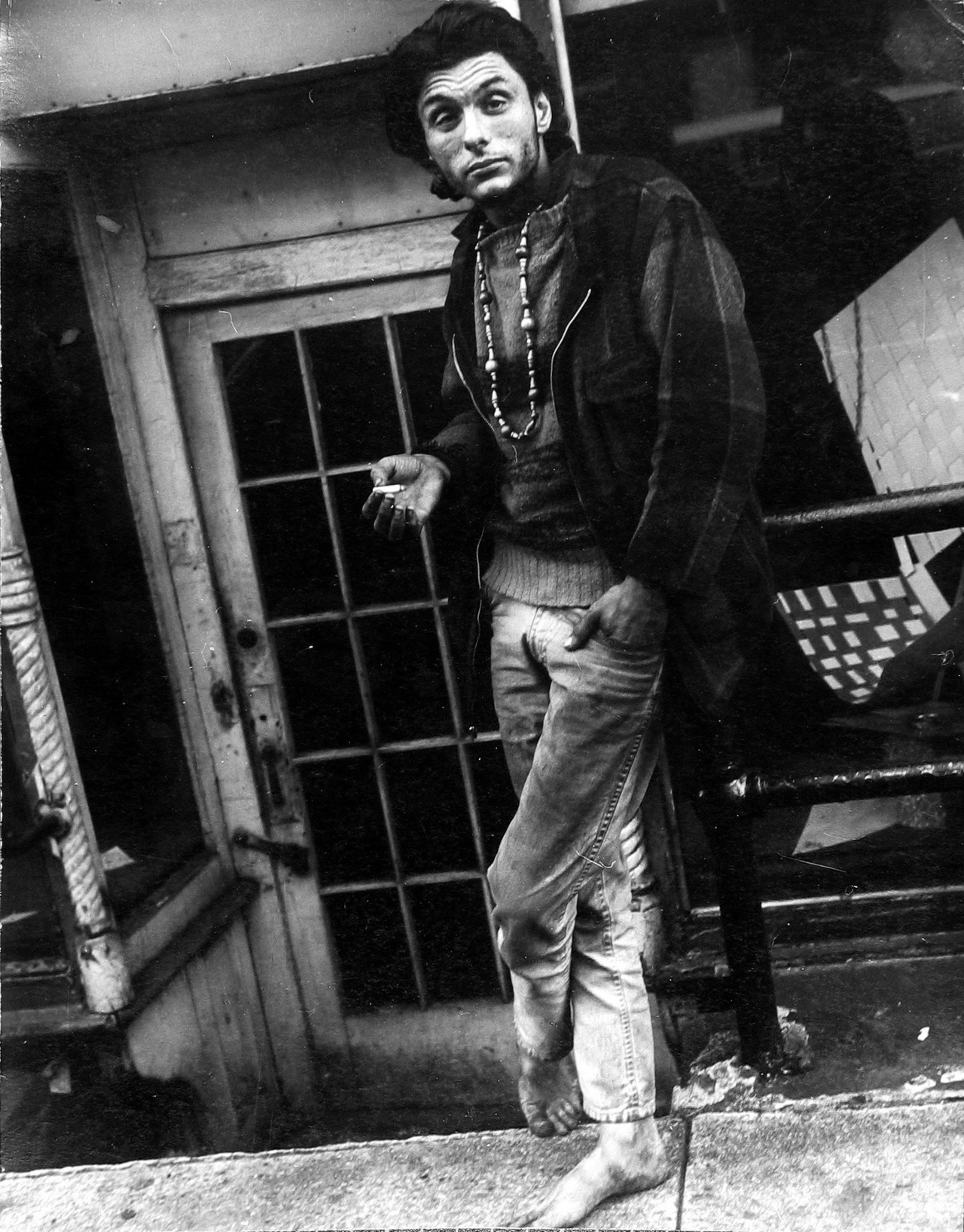 Barefoot Man Wearing Beads Smoking Outside DoorwayLeon Levinstein 