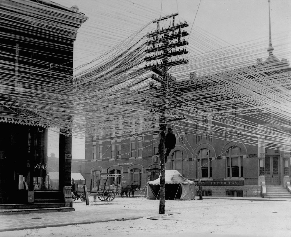 Unknown Photographer. View of a lineman working on power. Telephone lines at an intersection in Pratt, Kansas, USA, 1911.