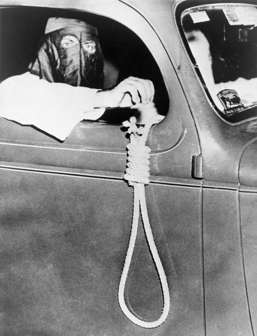 historicaltimes:Ku Klux Klan member holds a noose outside a car window during a parade through an Af