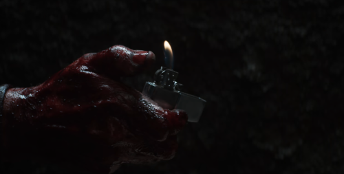 A bloody hand ignites a silver flip lighter.