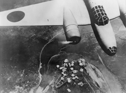 A Japanese bomber in flight (September 14th, 1940). Below, smoke rises from a cluster of bombs dropp