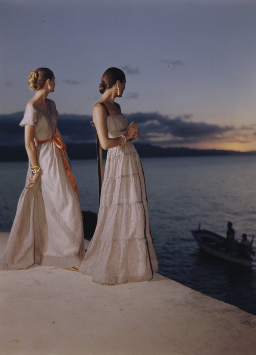 Two women in evening gowns posing on a terrace above a body of water at sunset, possibly in Puerto R