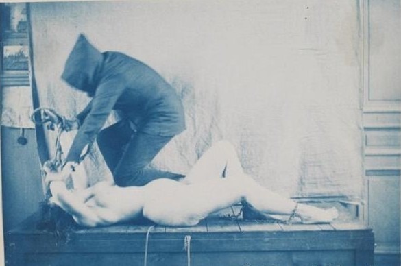 Femme nue, un personnage vêtu et le visage caché par une capuche en train de lui