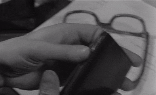 A scene from La Peau Douce of hands opening a day planner and pulling out a top half of a matchbook from behind a flap with the name "Nicole" and a phone number written on it.