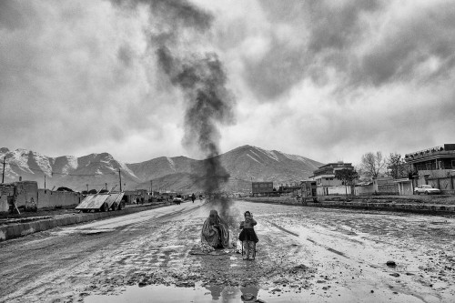 Kabul.A woman wearing a burqa, with a young girl, sit in the middle of a muddy road in front of a bo