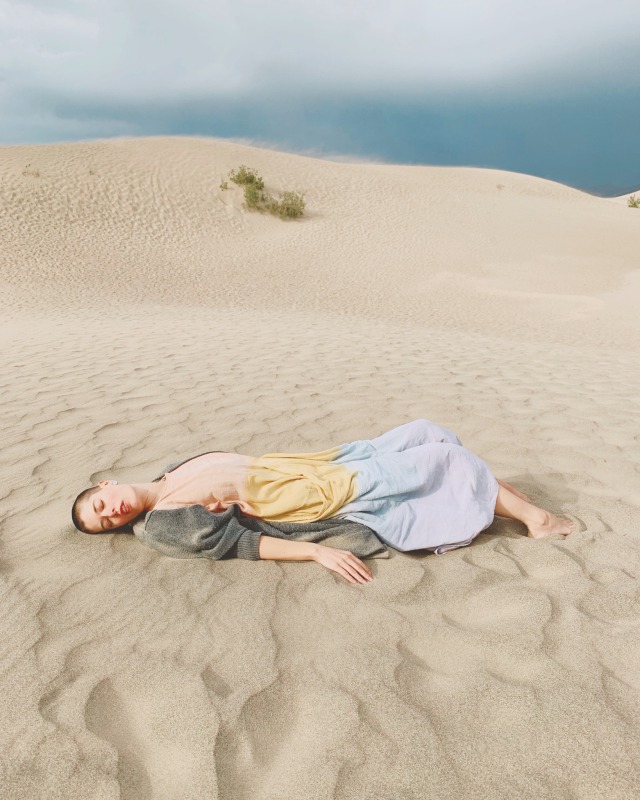 person in pastel coloured caftan lying on a sand dune in the sun with a dark stormy sky behind