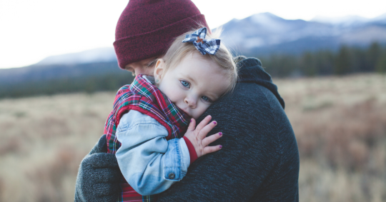 image of parent holding young child outside with mountains in the distance