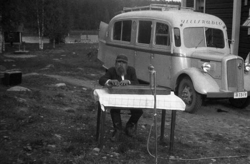 A Finnish man plays a kantele for a radio broadcast (the broadcast van can be seen in the background