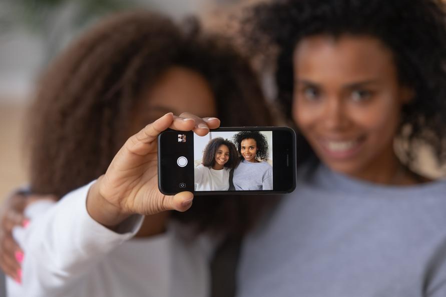 Two black friends with curly hair take a selfie on a mobile smartphone