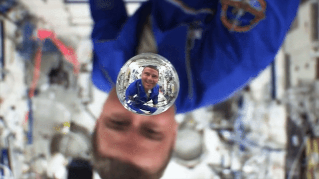 An astronaut floats upside down toward a water bubble aboard the International Space Station. His face is magnified and right side up in the liquid. Credit: NASA